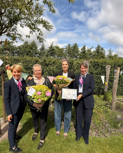 Twee winnaars van de fotowedstrijd met hun boeket en ingelijste winnende foto in de tuin.